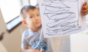 A smiling boy showing off his drawing