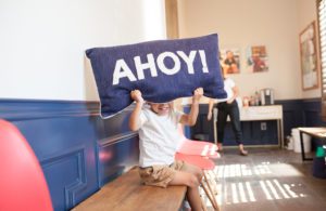 One of our kiddos playfully holding up a pillow with the word AHOY! on it