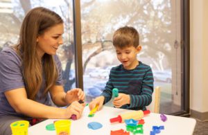 a staff member and a young boy playing with PlayDoh